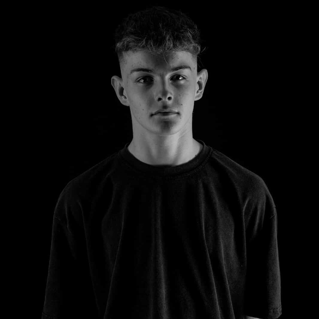 A young boy dressed in a black shirt is looking directly at the camera. The image is in black and white, highlighting the boy's facial expression and features.